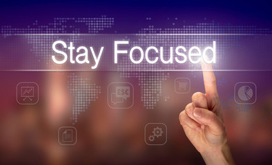 A hand selecting a Stay Focused business concept on a clear screen with a colorful blurred background.