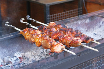 Tasty fried pieces of meat on skewers are roasted on grill at festival outdoor. Cooking meat on barbecue. Shish kebab national cuisine of Central Asia.