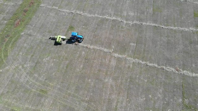 Harvester and tractor in field press grass into bundle, aerial view in Inner Mongolia prairie, China.