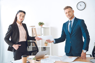 businesswoman giving document to colleague at workplace in office