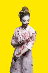 scary damaged girl in nurce halloween costume looking like zombie with syringe on yellow background