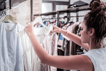 Dresses on hangers. Helpful assistant of fashion boutique putting new summer dresses on hangers...
