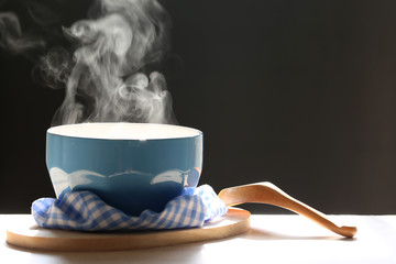 Selective focus of smoke rising with hot soup in cup and spoon on dark background