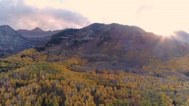 Sun peaking over mountain range covered in colorful foliage in the Wasatch Mountains during Fall.