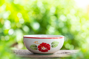 White empty ceramic bowl on wooden table with green blur light background. For photo montage