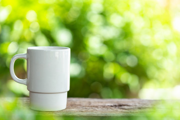 Coffee cup on wooden table or counter with green nature light blur background and space for text, design, photo montage or advertising