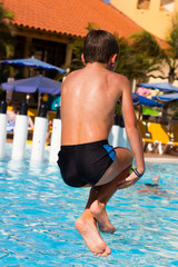 Naklejka premium Young boy diving into swimming pool. Kid holding legs in the air jumping into water. Summer vacation, resort fun holidays, leisure time concepts