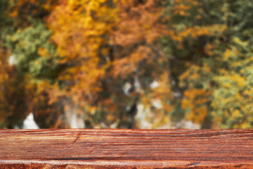 Naklejka na ściany i meble Autumn bokeh background with wooden plank in focus. Blurred fall nature with brown table