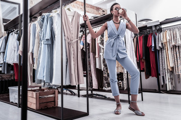 Before fitting room. Woman shopping in fashion boutique drinking her coffee before going to fitting room