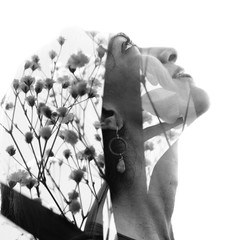 Double exposure portrait of a young smiling girl with flawless skin combined with delicate flower petals, in black and white