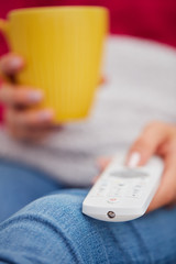 Girl holding TV remote and drinking coffee / tea on a couch.