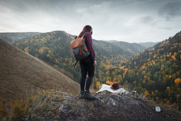 Young girl with backpack and hat in trekking boots on the background of autumn nature