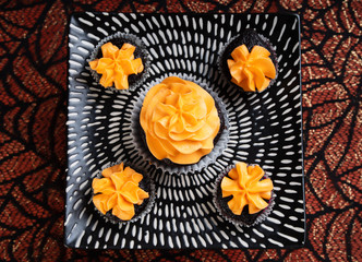 Top view of five Halloween chocolate cupcakes with orange frosting on a black and white patterned plate