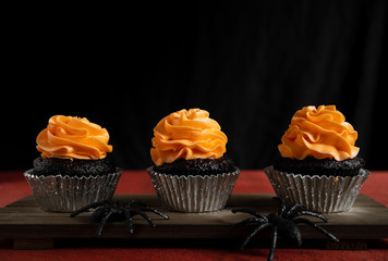 Three Halloween chocolate cupcake with orange frosting on a wooden tray with spiders