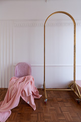 Composition of oldrose blanket setting on mid century modern chair in baby pink color setting in white wooden stripe and classic moulding wall and gold clothes hanger.  