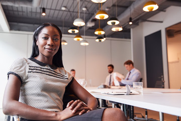 Portrait Of Businesswoman In Modern Boardroom With Colleagues Meeting Around Table In Background