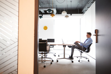 Businessman Working On Laptop At Boardroom Table Viewed Through Meeting Room Door