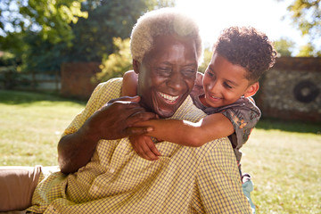Senior black man sitting on grass, embraced by his grandson - Powered by Adobe