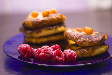 Baked cottage cheese with red raspberries and orange sea buckthorn on a purple plate.