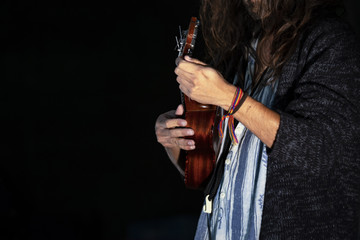 Musician with long hair on stage does a performance playing a small ukulele.