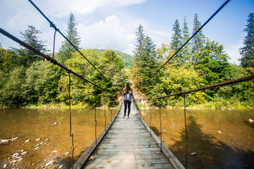 Tourist woman walk by long wooden suspension bridge above river. balance concept