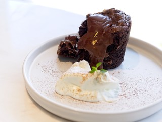 chocolate brownie lava cake and melted chocolate served with whip cream on white round plate on white marble table