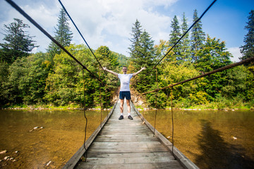 Fototapeta premium Tourist man walk by long wooden suspension bridge above river. balance concept
