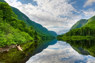 Fototapeta na wymiar Vibrant green forest and still waters of Jacques Cartier river on a warm summer day, Jacques cartier national park, Quebec, Canada