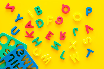 Alphabet for kids concept. English letters in disorder near stencil on yellow background top view