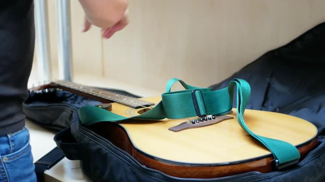 Guitar player folds acoustic guitar in a black case after the concert