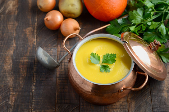 Homemade pumpkin soup in casserole on wooden background, selective focus.