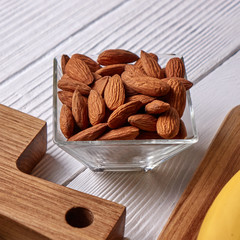 Close-up of almond nuts in a glass bowl on a wooden board on a gray wooden background. Vegetable protein for vegans.