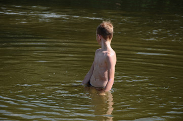 The boy is bathing on the river.