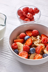 Homemade natural breakfast with granola, strawberries, almonds, blueberries, raspberry, fresh soy milk in a bowl on a wooden background