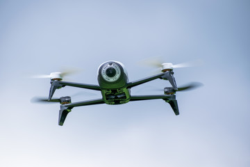 Black camera drone in flying with visible propellers movement and in  blue sky background