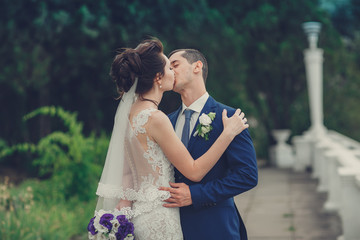 elegant stylish groom with his happy gorgeous brunette bride on the background of trees in the park