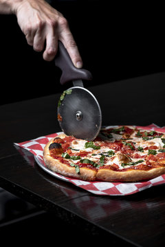 Man's hand cutting pizza on cloth