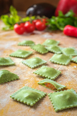raw green homemade ravioli with spinach and vegetable on wooden table with flour