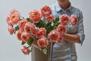 A bouquet of fresh pink roses in a brown vase holds a girl in her hands