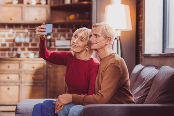 Obraz premium Selfie time. Inspired aged spouses sitting together and taking selfies at home
