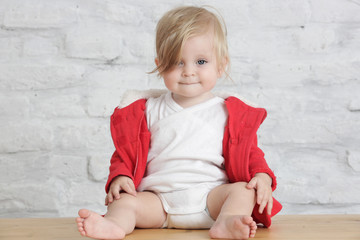 Fototapeta premium Indoor portrait of a cute blond baby in the red and white outfit 