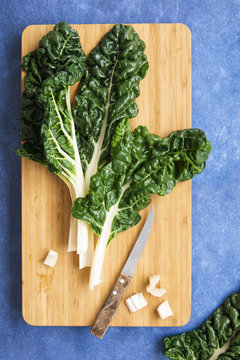 Silverbeet leaves trimmed with a knife on a chopping board.