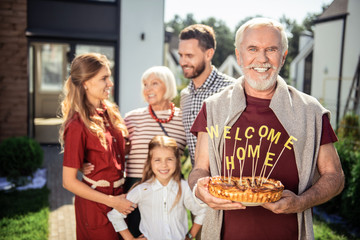 Keep smiling. Pleased pensioner holding cake in both hands while waiting for guests