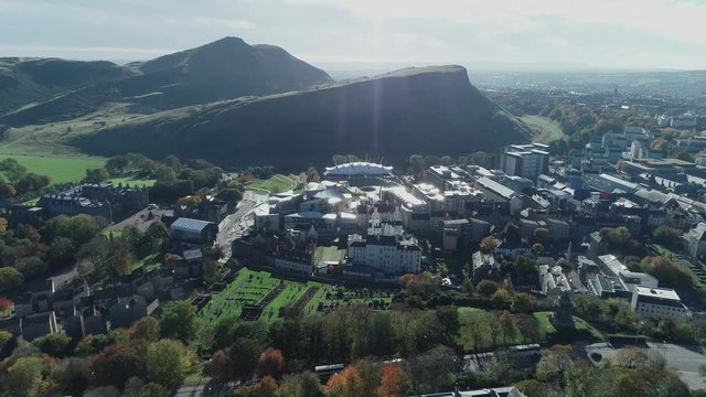 Aerial footage above Calton Hill. Flying right with view to Arthurs Seat, Salisbury Crags, Holyrood Palace and the Scottish Parliament.