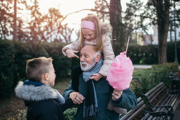 Happy grandfather having fun with his grandchildren in city park.