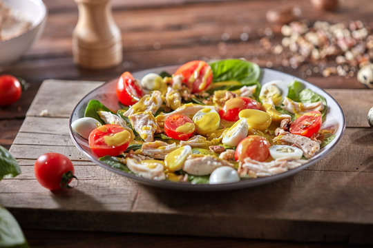 Fresh homemade salad with natural ingredients - organic clean vegetables, chicken meat and guail eggs, spicy mustard in a plate on a wooden board.