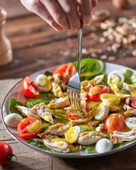 Woman hand holds a fork with freshly prepared dietary vegetarian salad with natural organic vegetables on a wooden table.