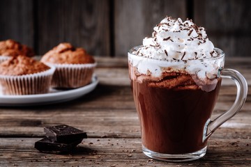 Hot chocolate drink with whipped cream in a glass on a wooden background