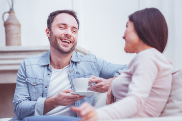 Hilarious. Portrait of optimistic bearded man smiling broadly while talking with his adorable wife and expressing delight on his face