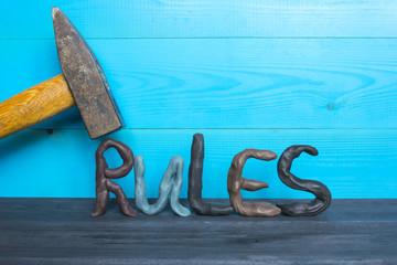 Breaking the rules concept, plasticine letters and a hammer on the blue background.